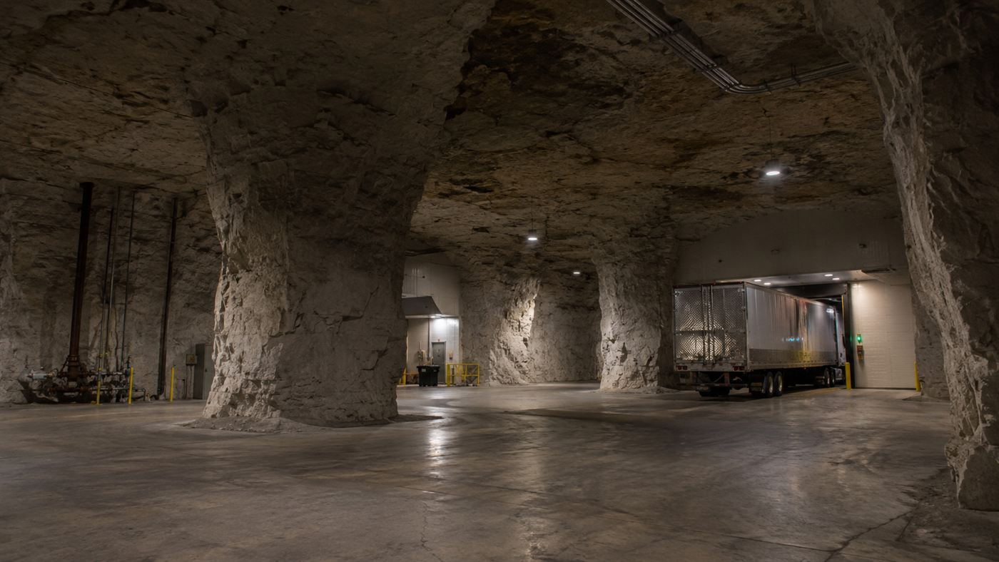 A semi-truck backed into a warehouse loading dock inside an underground limestone tunnel complex