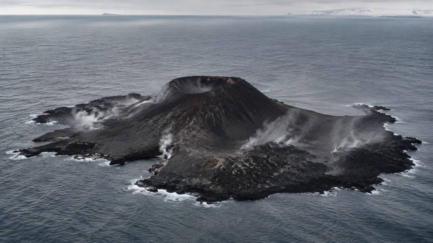 The barren dark volcanic island of Surtsey with a cinder cone rising from a grey ocean off Iceland