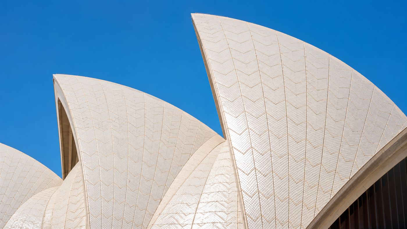Close-up of the gleaming white tiled shells of the Sydney Opera House curving against a clear sky
