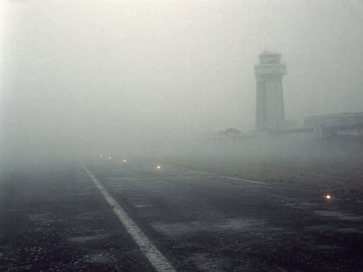 Thick Atlantic sea fog blanketing the Los Rodeos Airport runway in Tenerife showing near-zero visibility conditions with the runway lights barely visible through the mist, the 1977 aviation safety failure environment