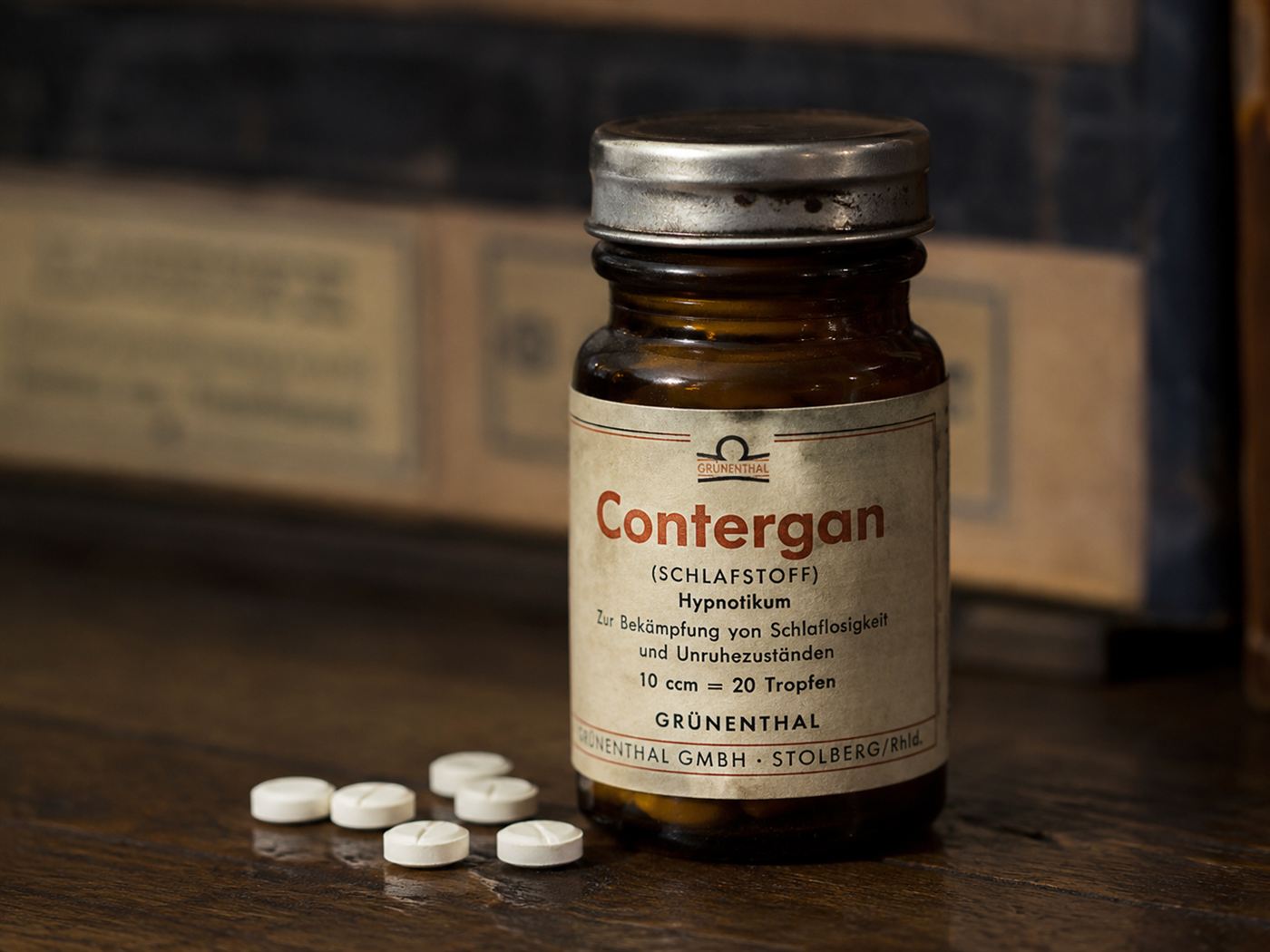 A vintage 1950s Contergan thalidomide pill bottle from West Germany with original German language label, placed on a dark wooden surface in dramatic directional light