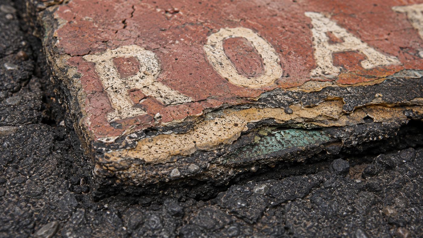 Extreme close-up of the layered, cracked surface and crooked letters of a handmade road tile