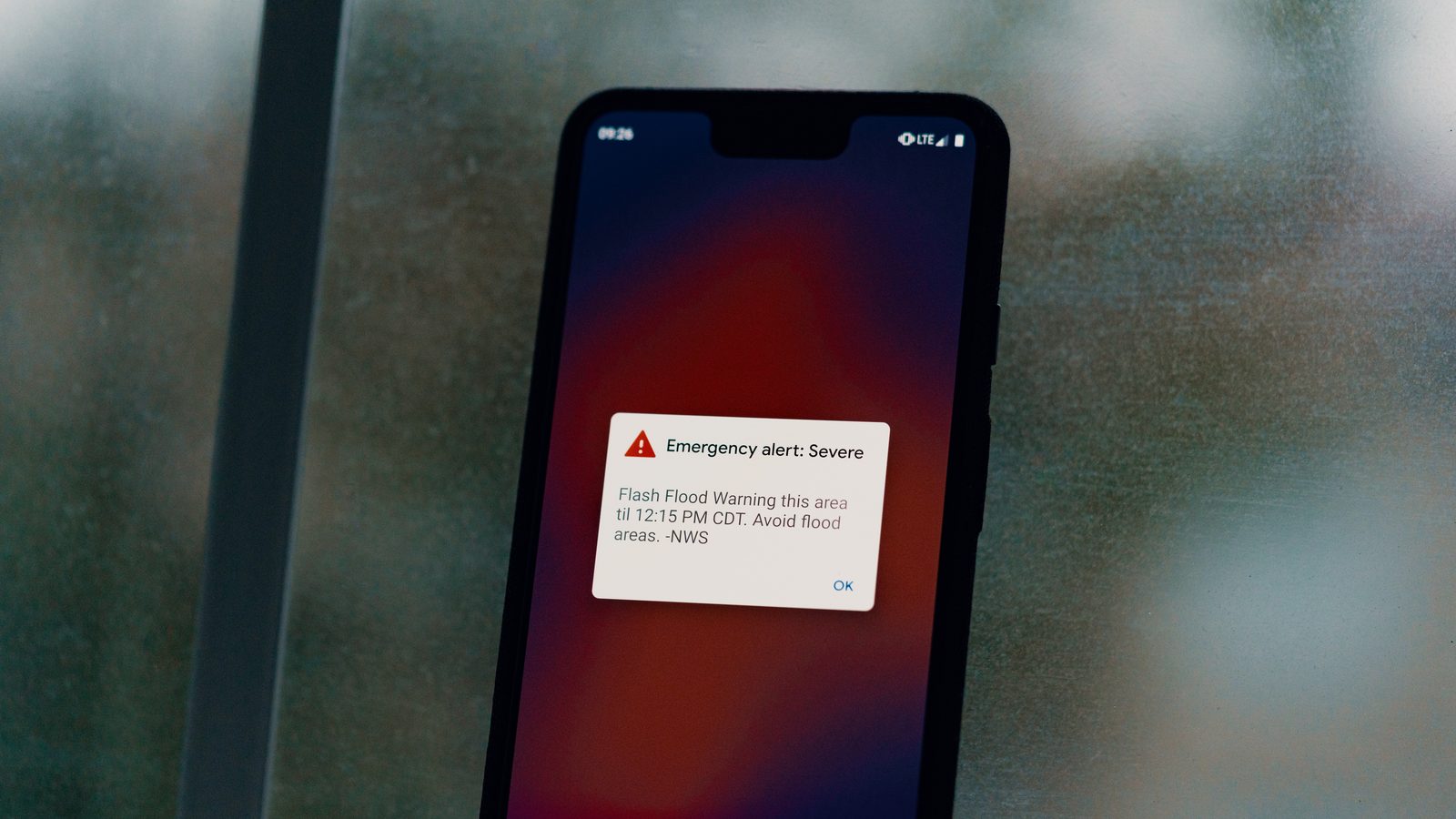 Celular com alerta de emergência de enchente na tela durante uma tempestade, exemplo de aviso de tempestade no WhatsApp ou no celular que vale conferir