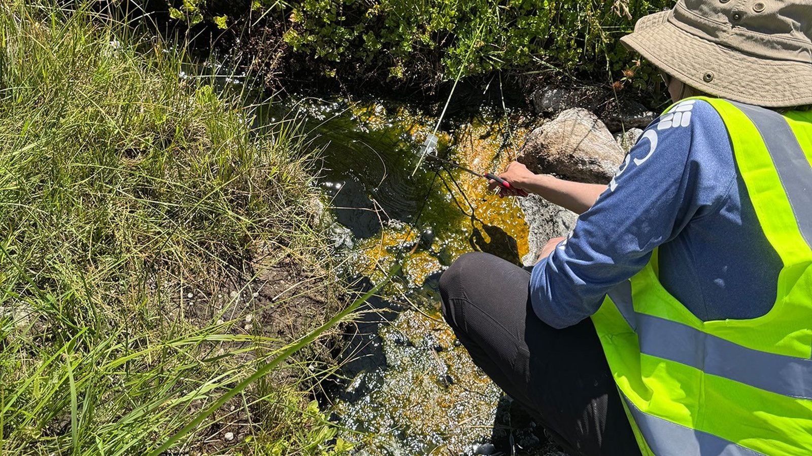Pesquisadora de colete coleta amostras em riacho de água quente onde vive a ameba do fogo, no Parque Vulcânico Lassen