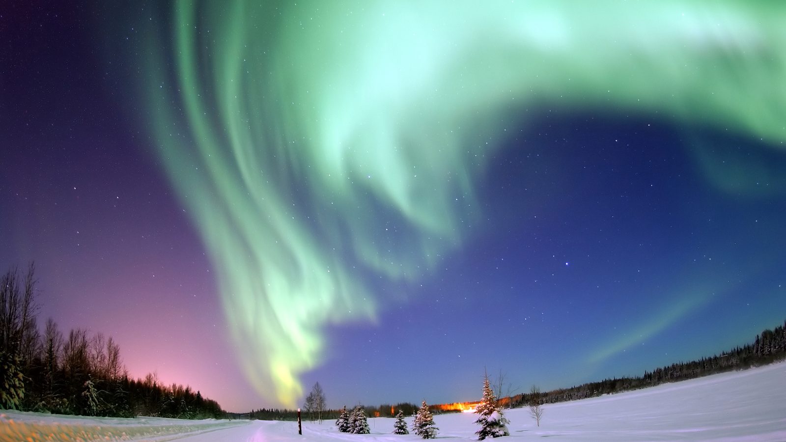 Aurora verde em cortina sobre estrada nevada e pinheiros no Alasca, ilustração de tempestade geomagnética G2 como a prevista pela NOAA