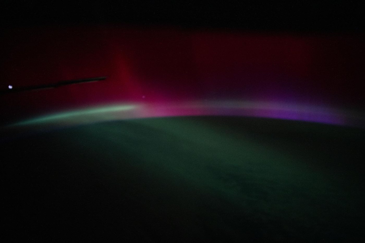 Aurora em faixas vermelha, roxa e verde sobre a curva da Terra, fotografada da Estação Espacial Internacional à noite