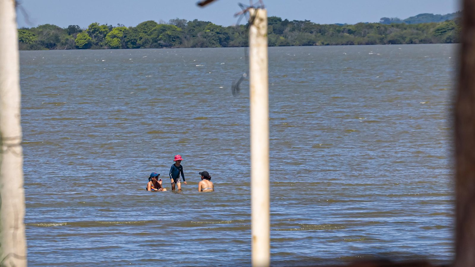 Banhistas se refrescam nas águas do Guaíba em Porto Alegre num dos dias das ondas de calor, vistos entre postes de madeira