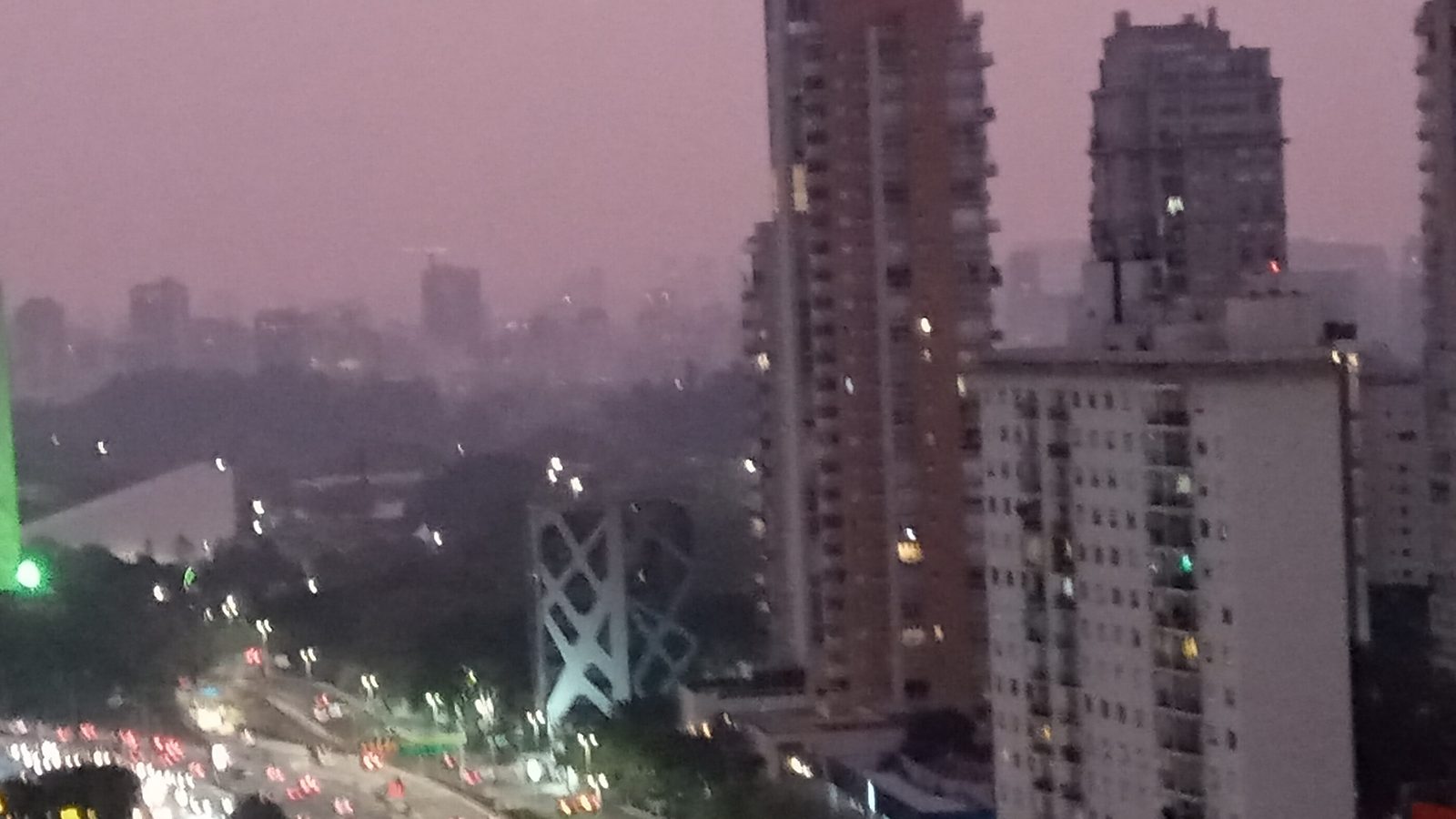 Avenida de São Paulo ao anoitecer com prédios e céu cinza-rosado encobertos pela fumaça das queimadas em 8 de setembro de 2024