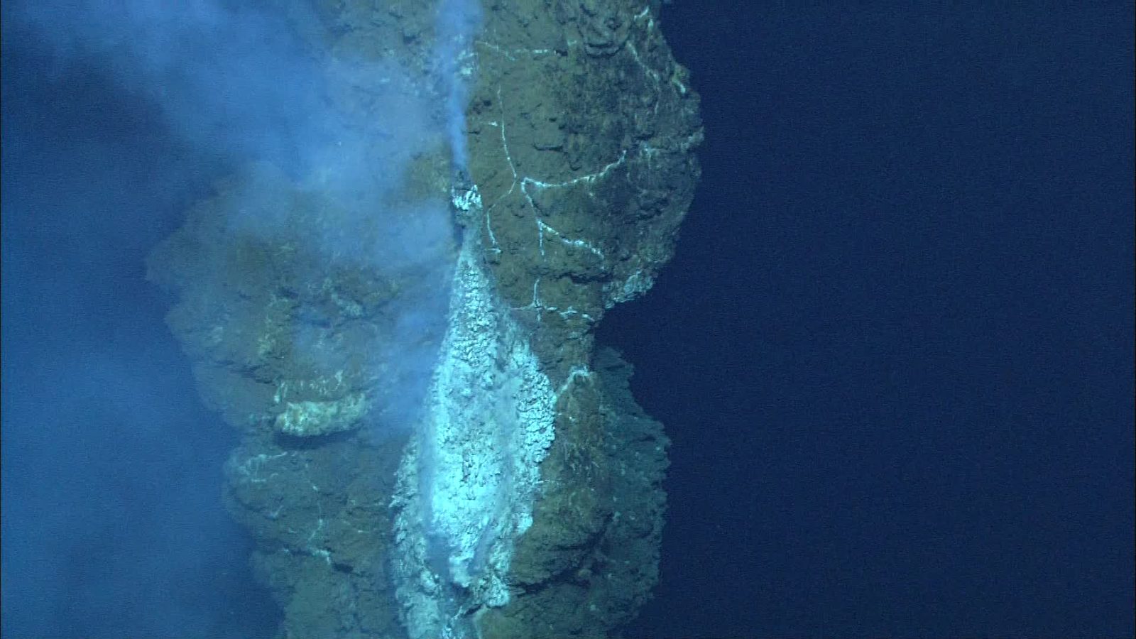 Chaminé de rocha no fundo do oceano soltando fluido quente em água azul escura, uma das fontes de por que o mar é salgado