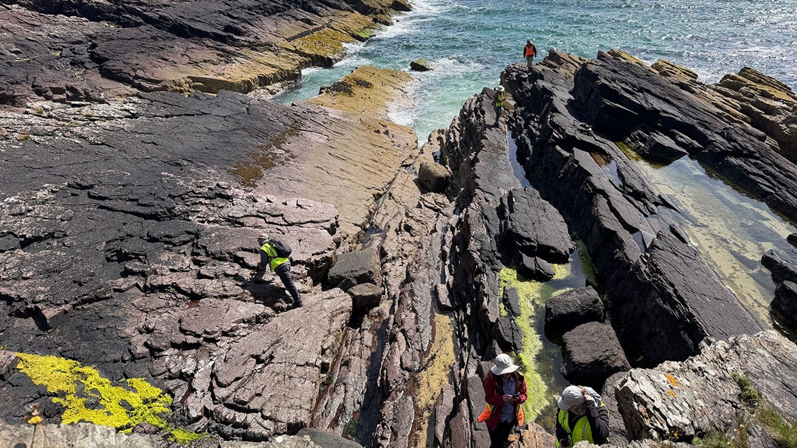 Cientistas da NASA caminham entre rochas escuras à beira-mar em Stoer, na Escócia, em busca de pistas sobre vida em Marte