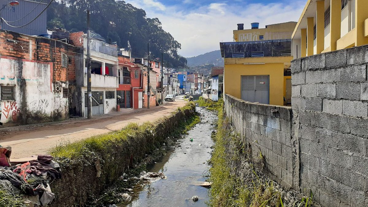 Córrego estreito com lixo nas margens entre casas e muros numa área urbana, um dos riachos da Grande São Paulo que perdem a cadeia alimentar