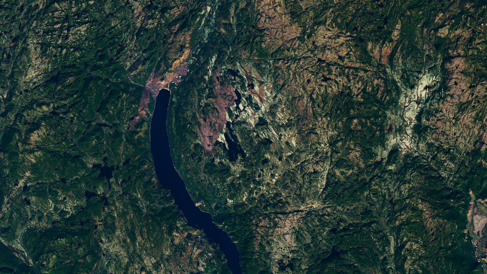 Imagem de satélite de uma região de floresta e rochas no Quebec, com um lago comprido e curvo à esquerda, na área da cratera de impacto de Uhackatik