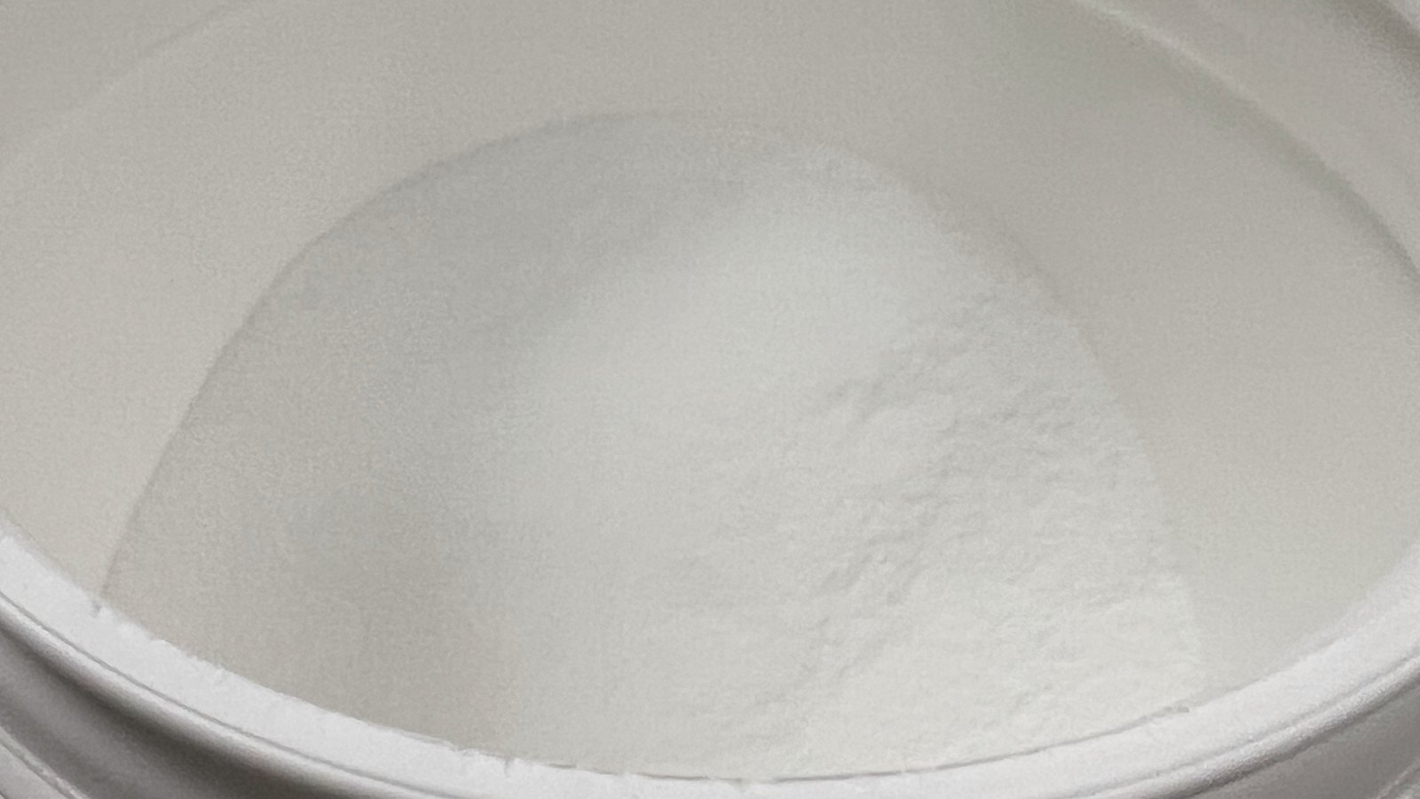 Creatina monohidratada em pó branco dentro de um pote aberto, visto de cima