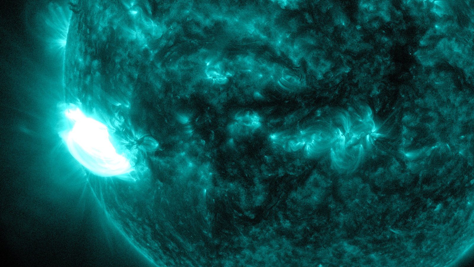 Disco do Sol em ultravioleta, tingido de verde-azulado, com o clarão branco de uma erupção solar na borda esquerda