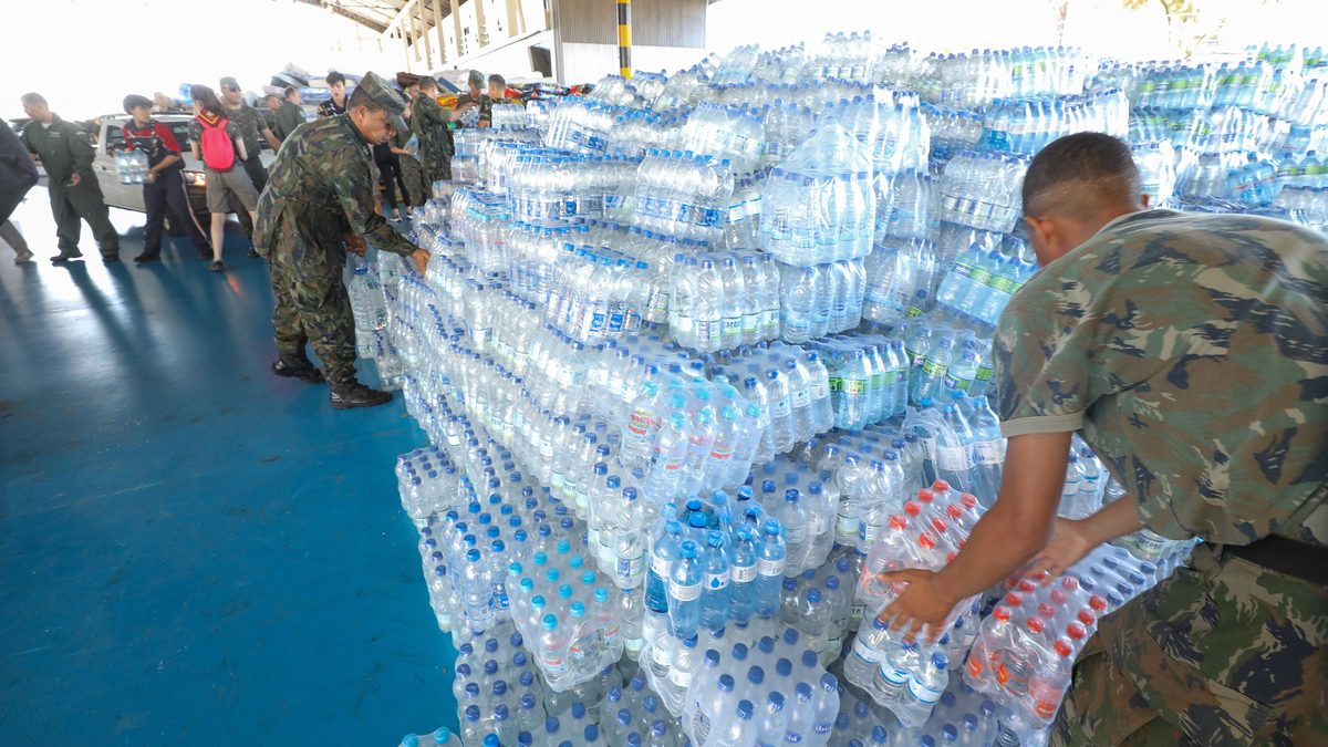 Militares empilham fardos de garrafas de água mineral doadas para as vítimas da enchente do Rio Grande do Sul, em hangar de Brasília