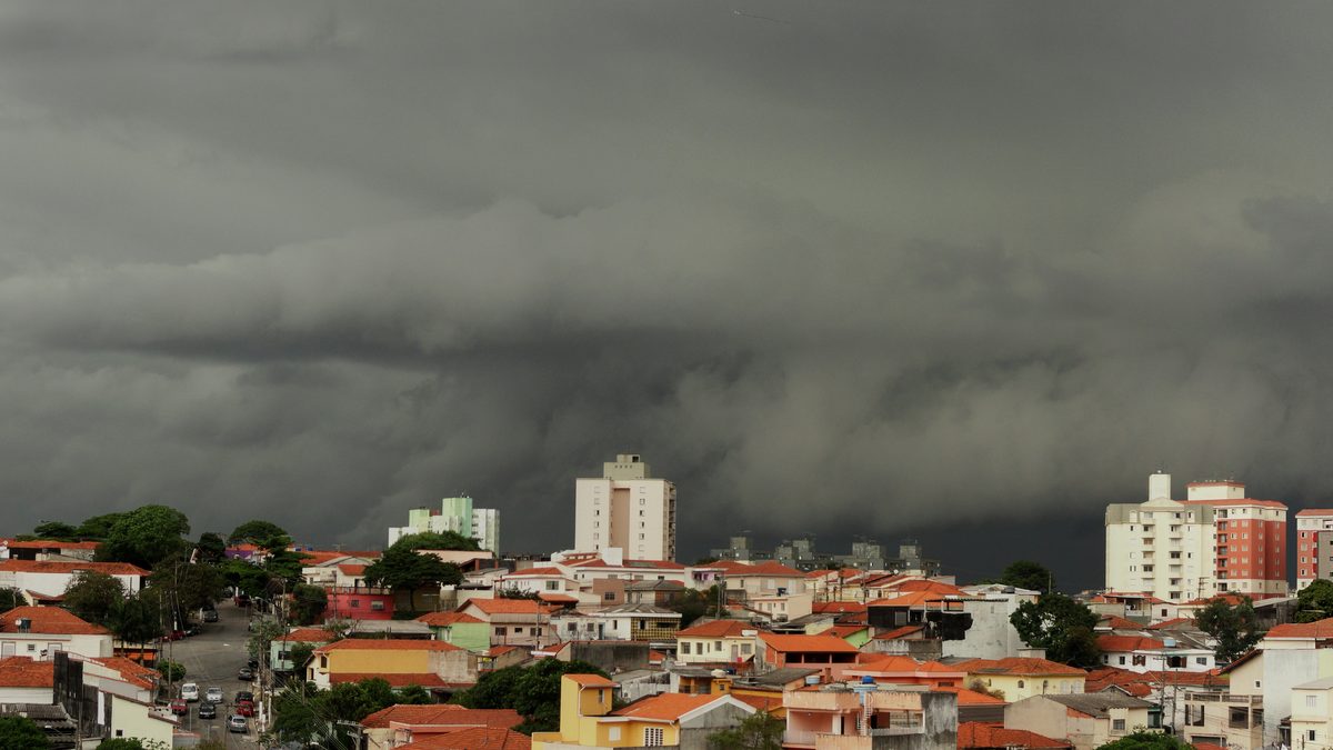 Trecho do panorama da tempestade de verão com a nuvem escura e baixa avançando sobre prédios e casas de São Paulo