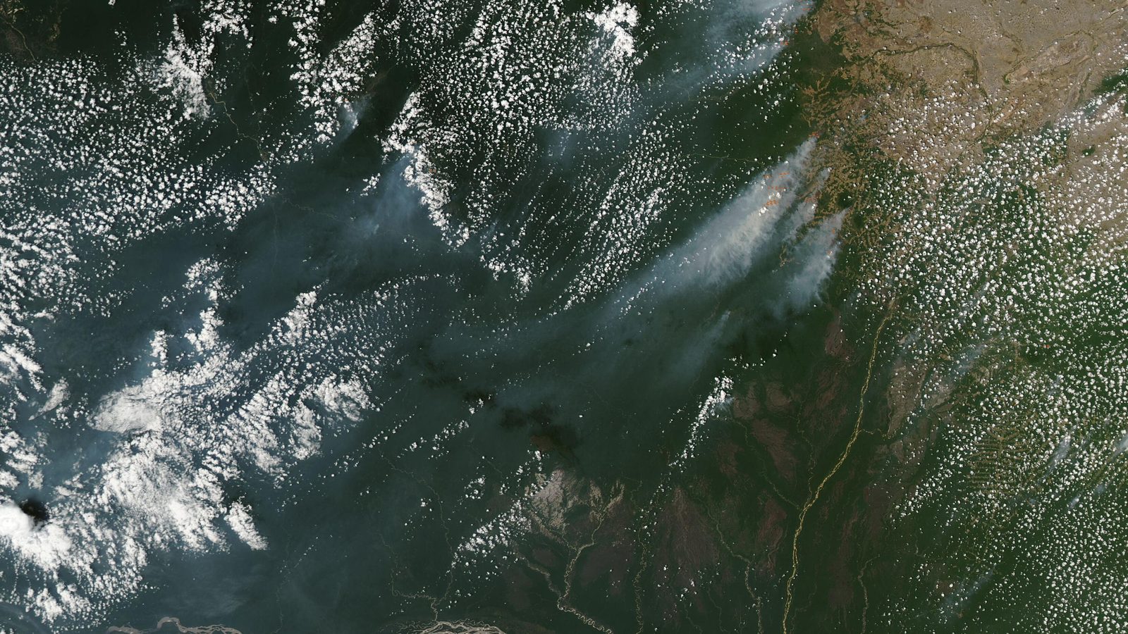 Imagem de satélite da NASA mostra plumas de fumaça de queimadas sobre a floresta amazônica, com rios sinuosos e nuvens