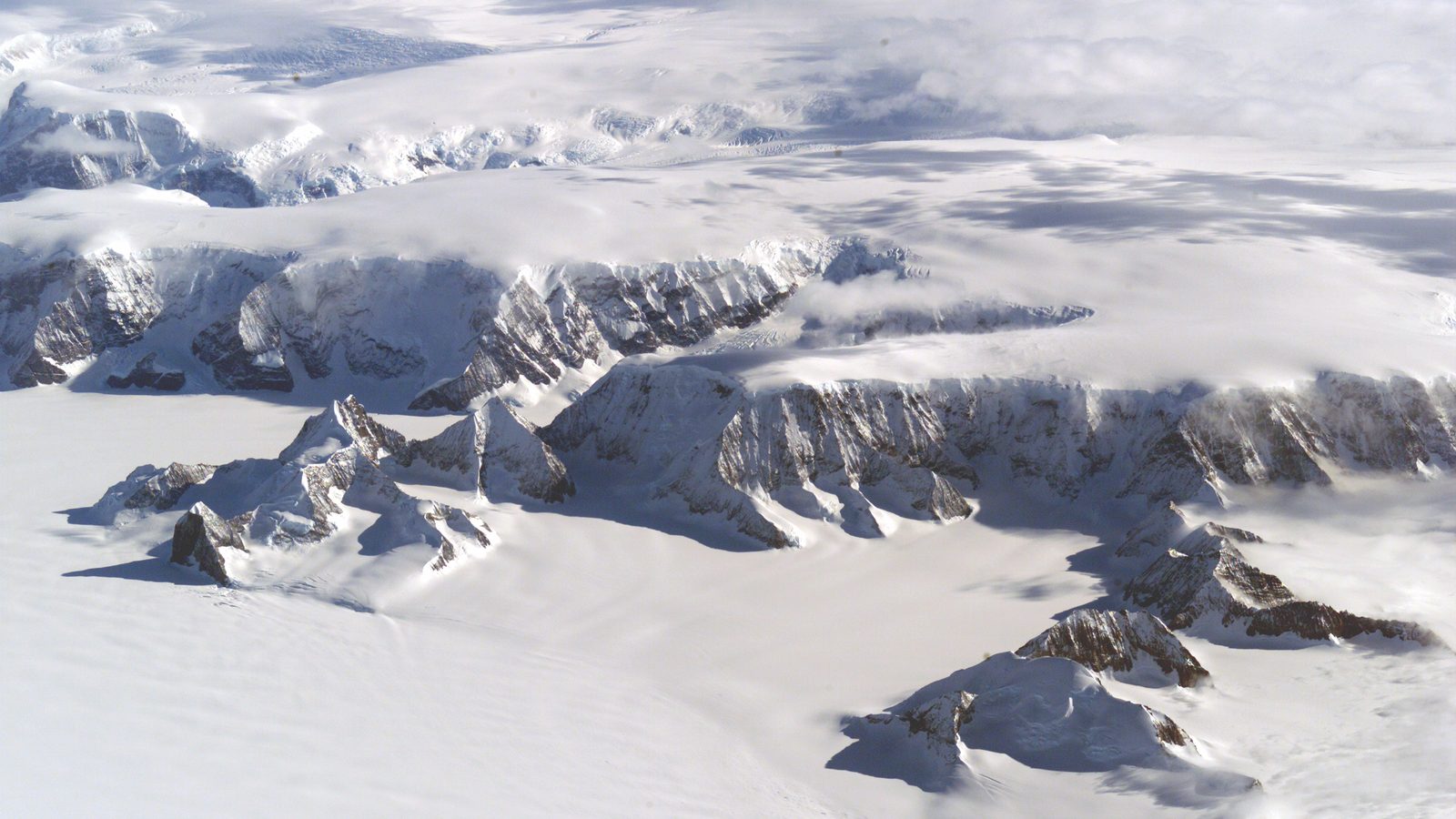 Vista aérea de montanhas rochosas escuras emergindo de um campo de gelo na Península Antártica, onde a perda de gelo na Antártica preocupa cientistas
