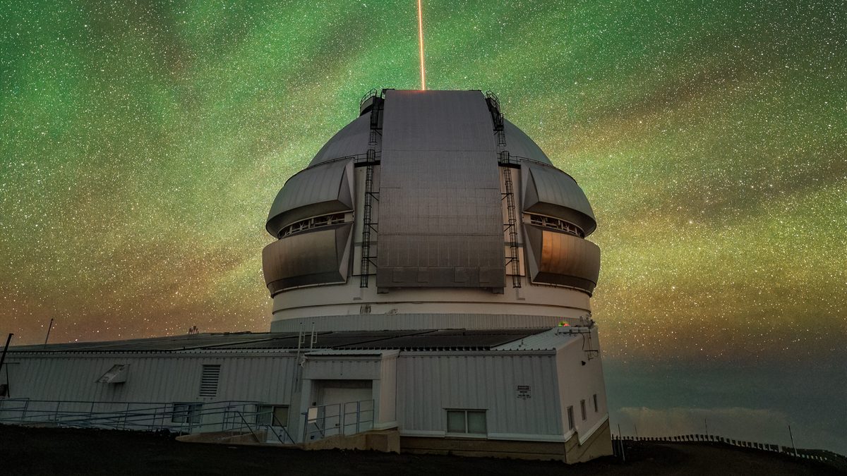 Cúpula do telescópio Gemini North em Maunakea com um feixe de laser laranja subindo para um céu verde de luminescência atmosférica