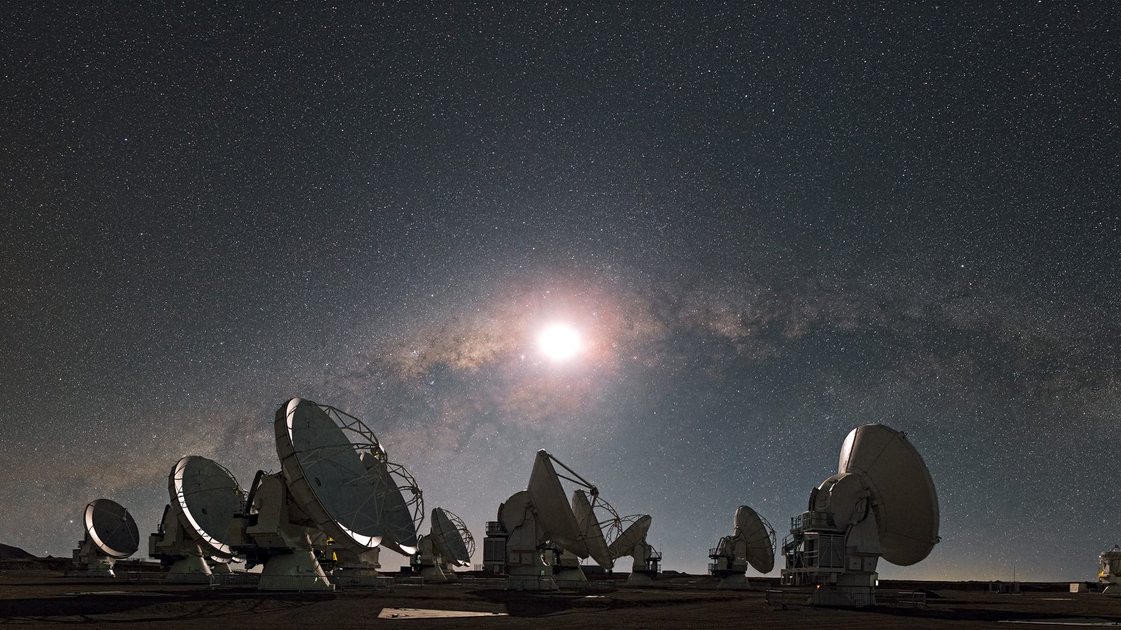 Lua brilhando sobre antenas do ALMA no Chile, com a Via Láctea e o céu estrelado ao fundo, no guia do céu de outubro