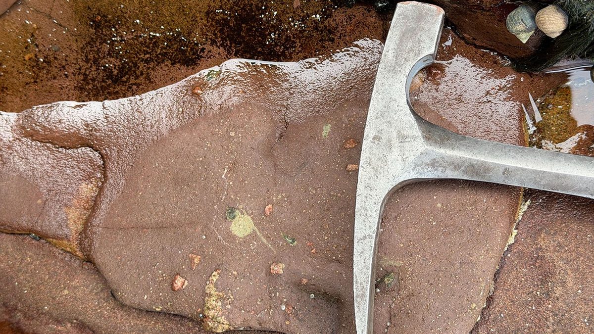 Arenito vermelho com manchas cinza-esverdeadas e martelo de geólogo na Baía de Stoer, rocha usada para entender vida em Marte