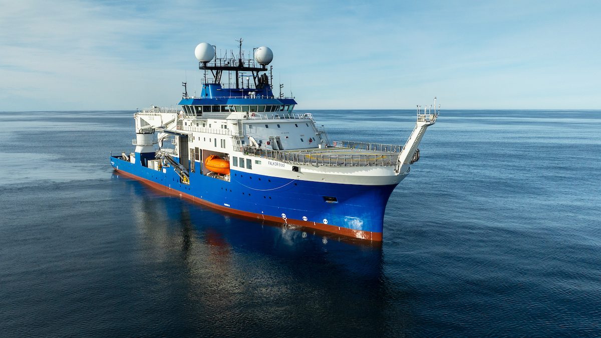 Navio de pesquisa azul e branco com duas antenas esféricas navegando em mar calmo sob céu claro