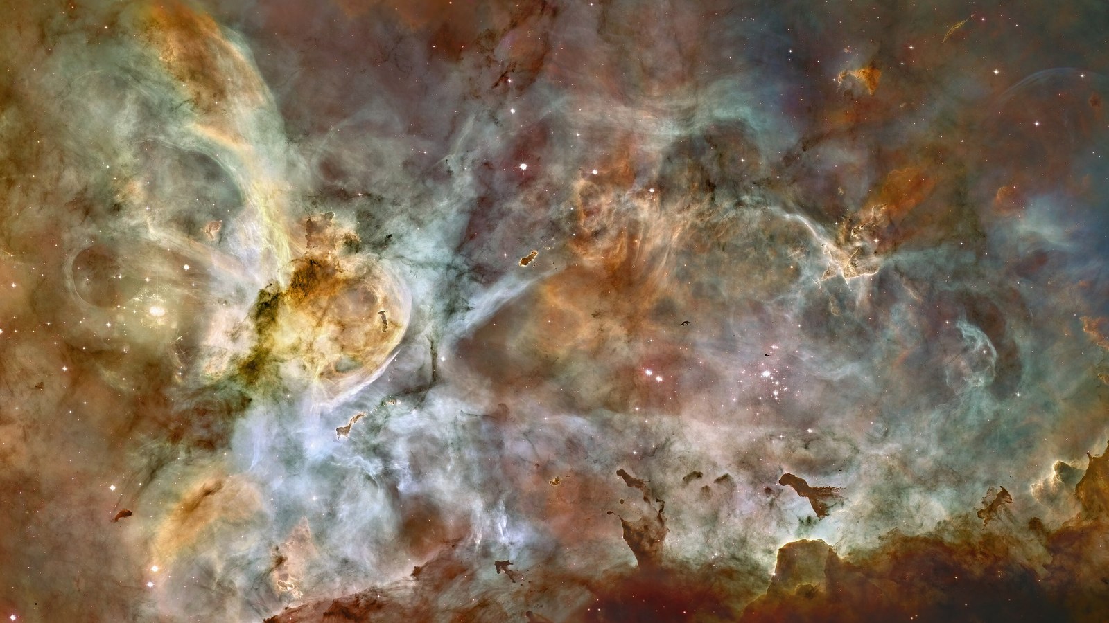 Nuvens de gás e poeira laranja, azul-claro e verde da Nebulosa de Carina em imagem do telescópio Hubble, com estrelas pequenas espalhadas