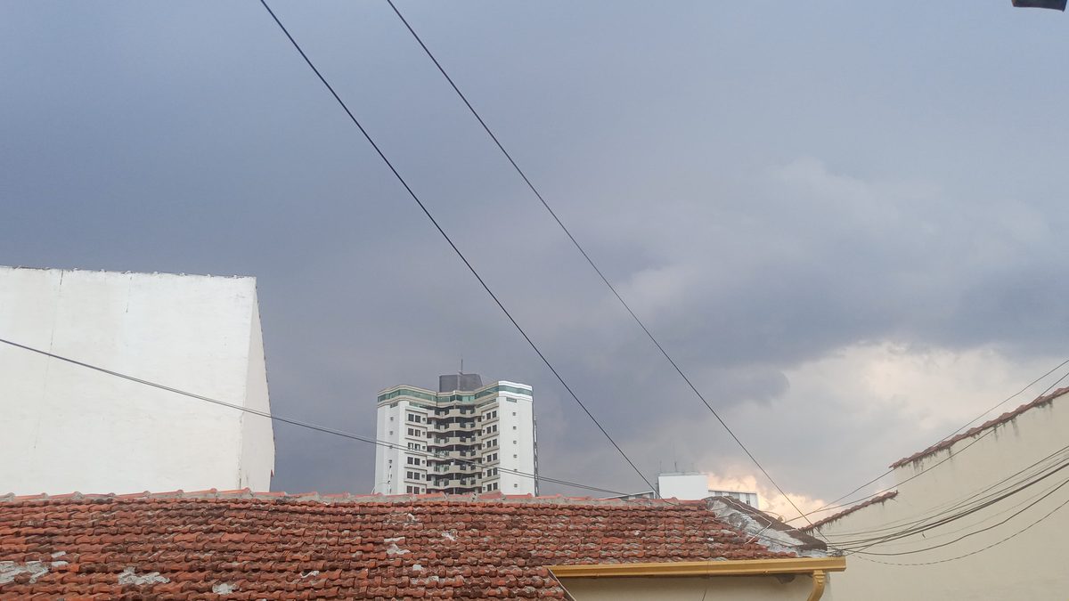 Nuvem escura e carregada sobre telhados e um prédio branco em Piracicaba, momentos antes da chegada de uma frente de rajada