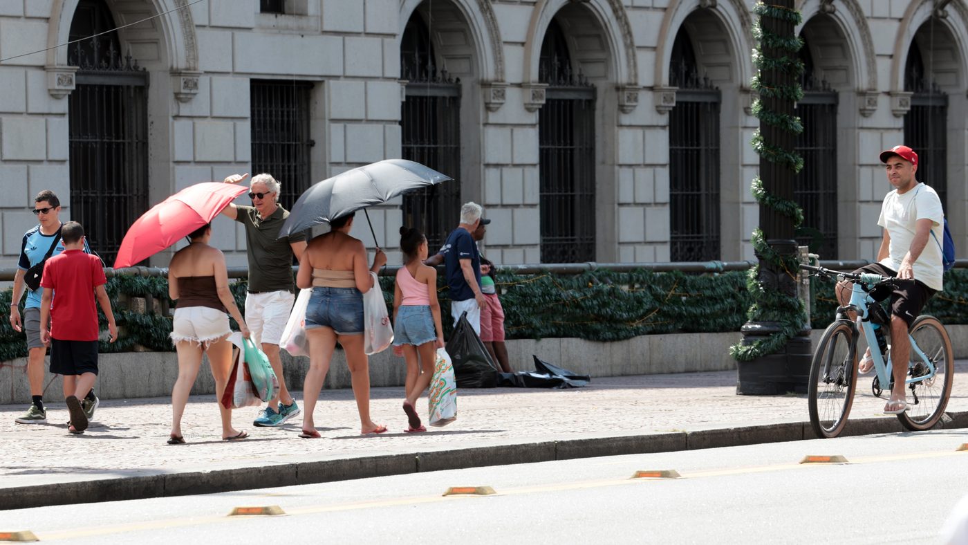 Alerta vermelho de onda de calor: pedestres se protegem do sol com guarda-chuvas numa rua de São Paulo