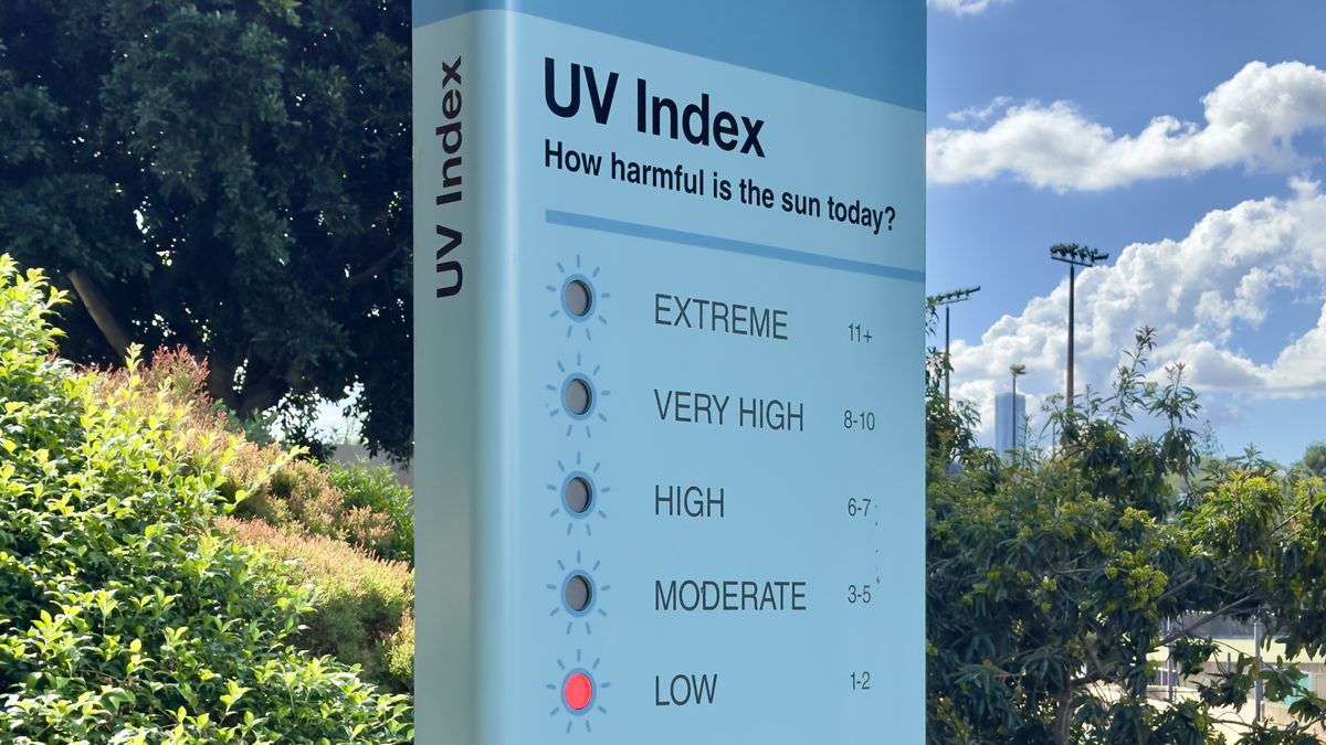 Painel azul com o título UV Index e as cinco faixas, de baixa a extrema, com a luz vermelha acesa na faixa baixa, sob céu claro com nuvens