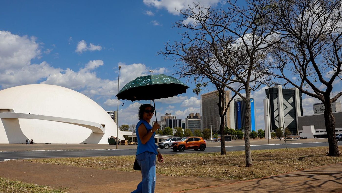 Mulher se protege do sol forte com uma sombrinha em Brasília, num dia em que o calor volta a pesar na capital