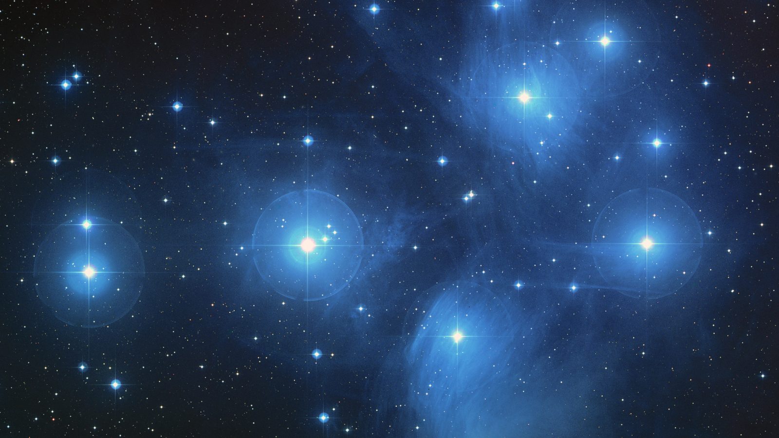 Aglomerado das Plêiades em imagem de telescópio, com estrelas azuis cercadas por névoa, as Sete Irmãs que a Lua visita em 27 de outubro