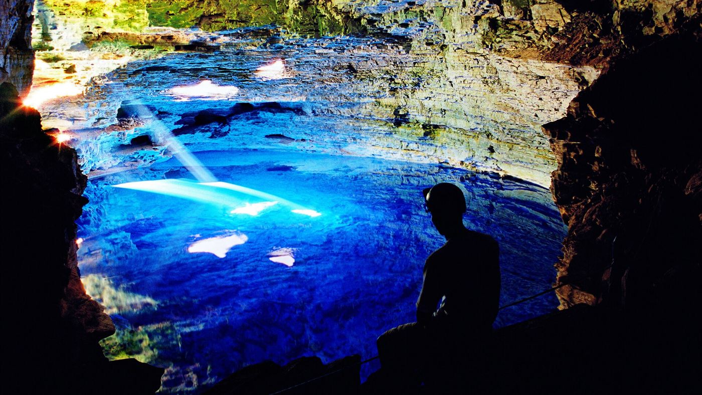 Facho de luz solar atravessa a entrada do Poço Encantado, na Chapada Diamantina, iluminando o lago azul turquesa