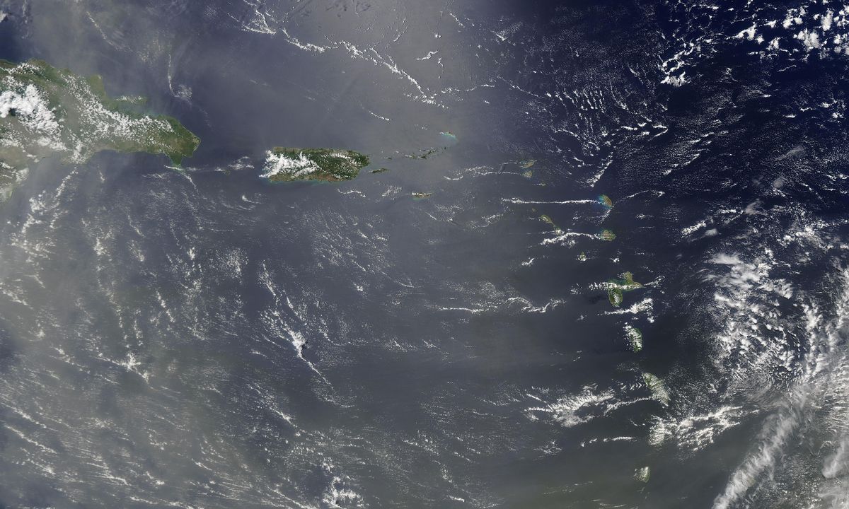 Mar do Caribe visto do espaço, com ilhas verdes e uma névoa bege de poeira sobre a água