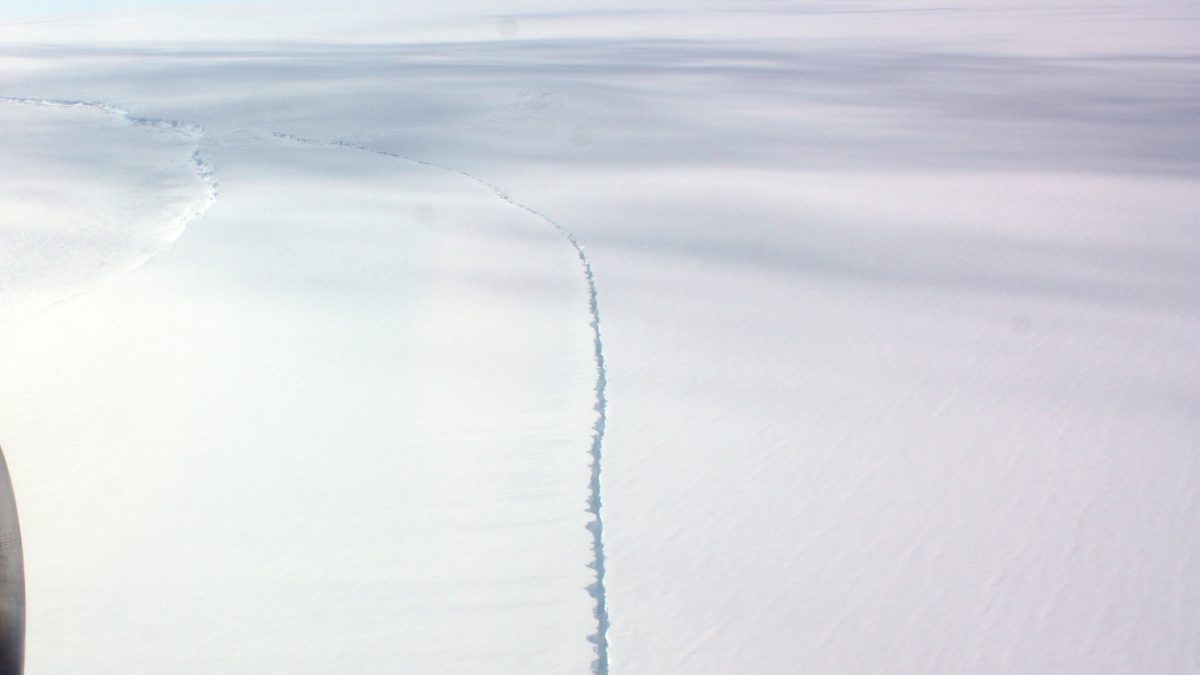 Rachadura fina cortando a superfície branca da plataforma de gelo Getz, na Antártica, vista da janela de um avião com as turbinas à esquerda