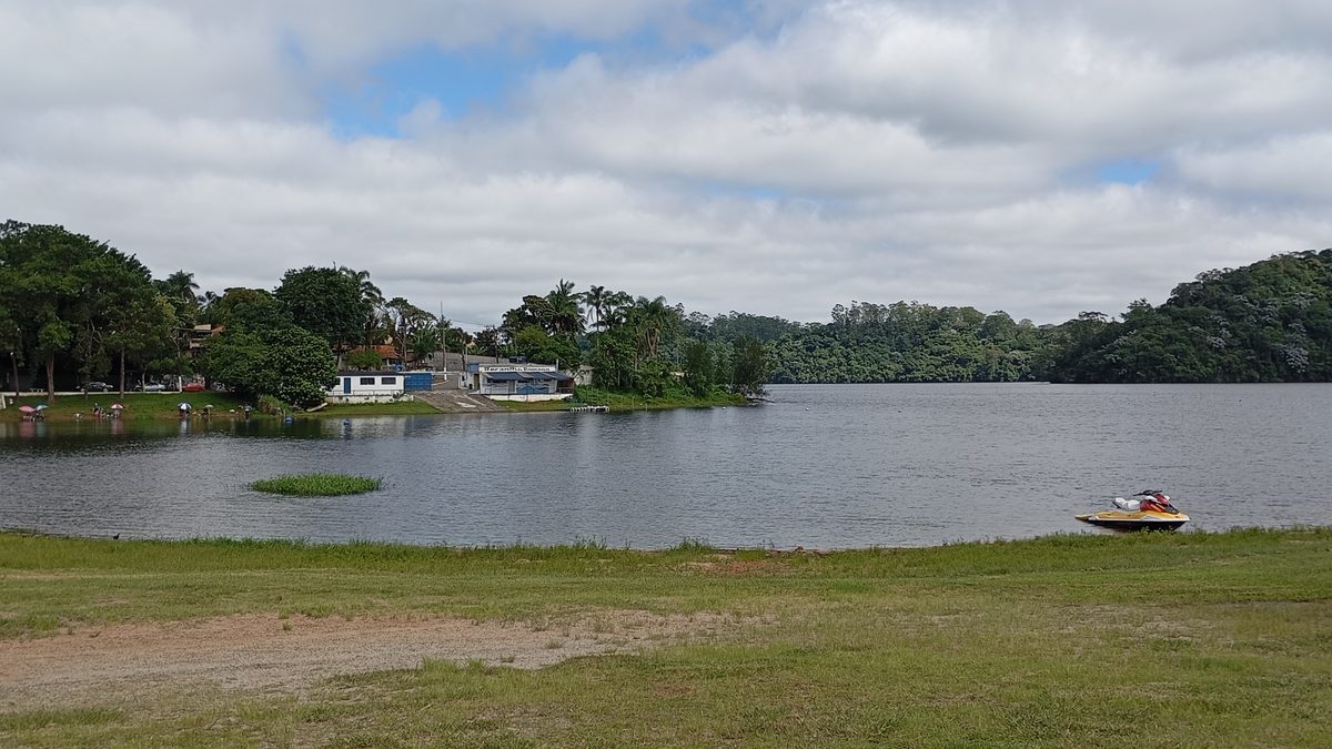 Represa Billings com margem gramada, mata ao fundo e uma moto aquática à beira da água