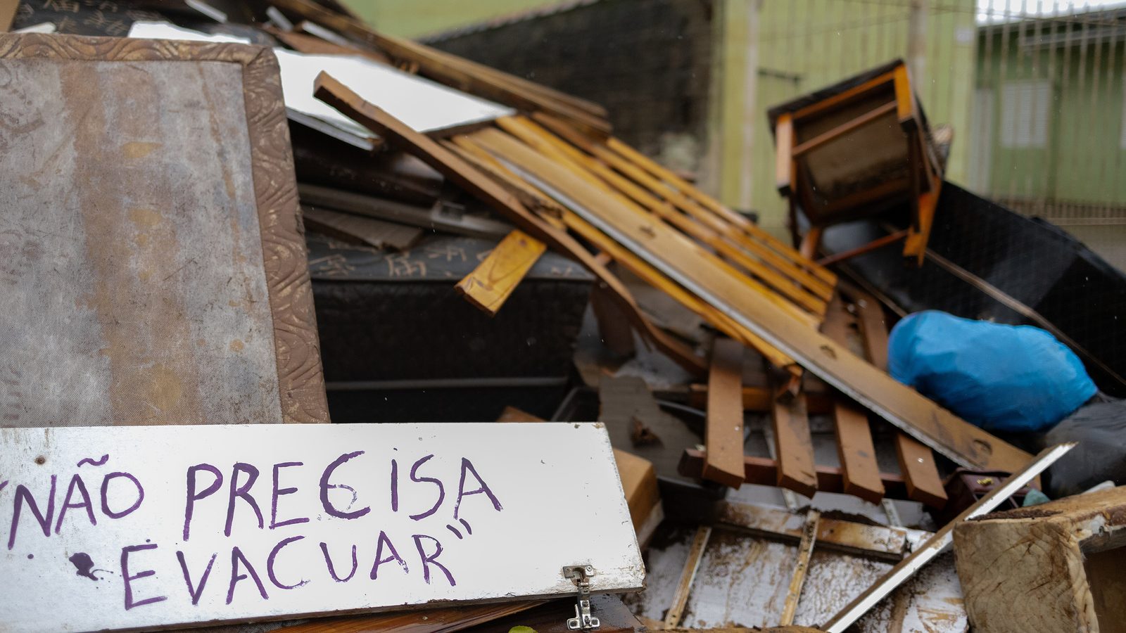 Placa escrita à mão com a frase não precisa evacuar sobre móveis destruídos pela enchente em Canoas, prejuízo que raramente tem seguro