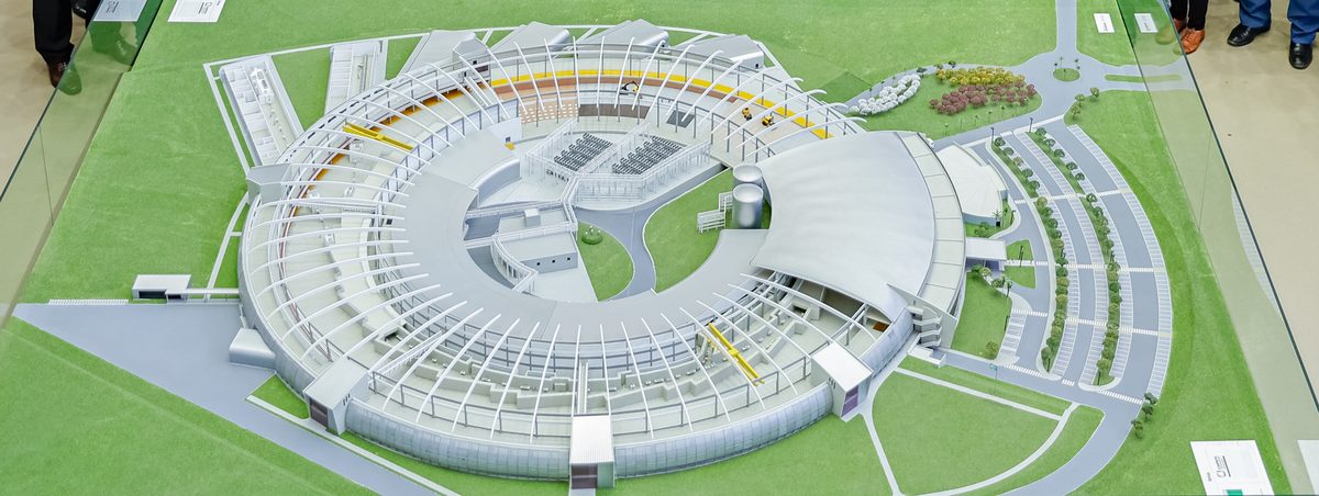 Maquete do Sirius vista de cima, com o prédio circular do acelerador de partículas cercado de gramado e vias de acesso
