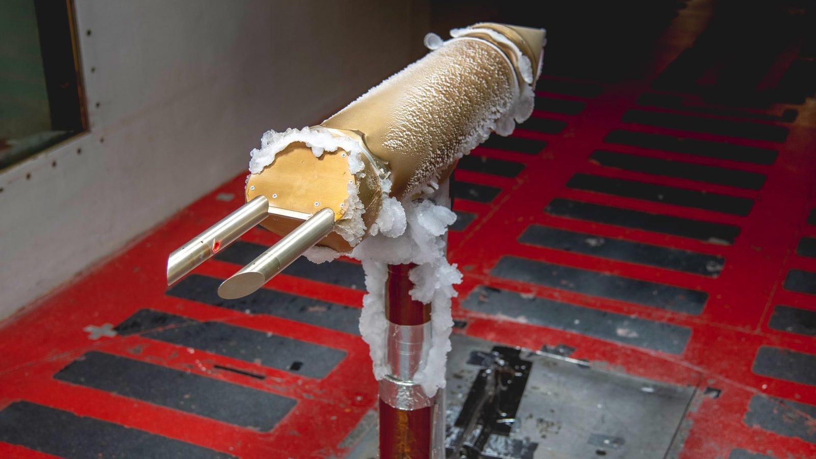 Sonda de metal dourado coberta de gelo branco dentro do túnel de gelo da NASA, usada para estudar gotas super-resfriadas