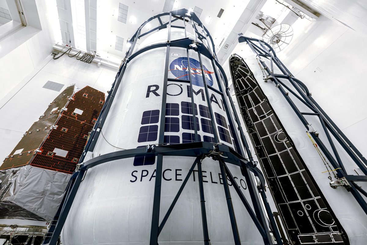 Telescópio Roman dentro da carenagem branca com o logotipo da NASA, em sala limpa do Kennedy, ao lado da outra metade da carenagem