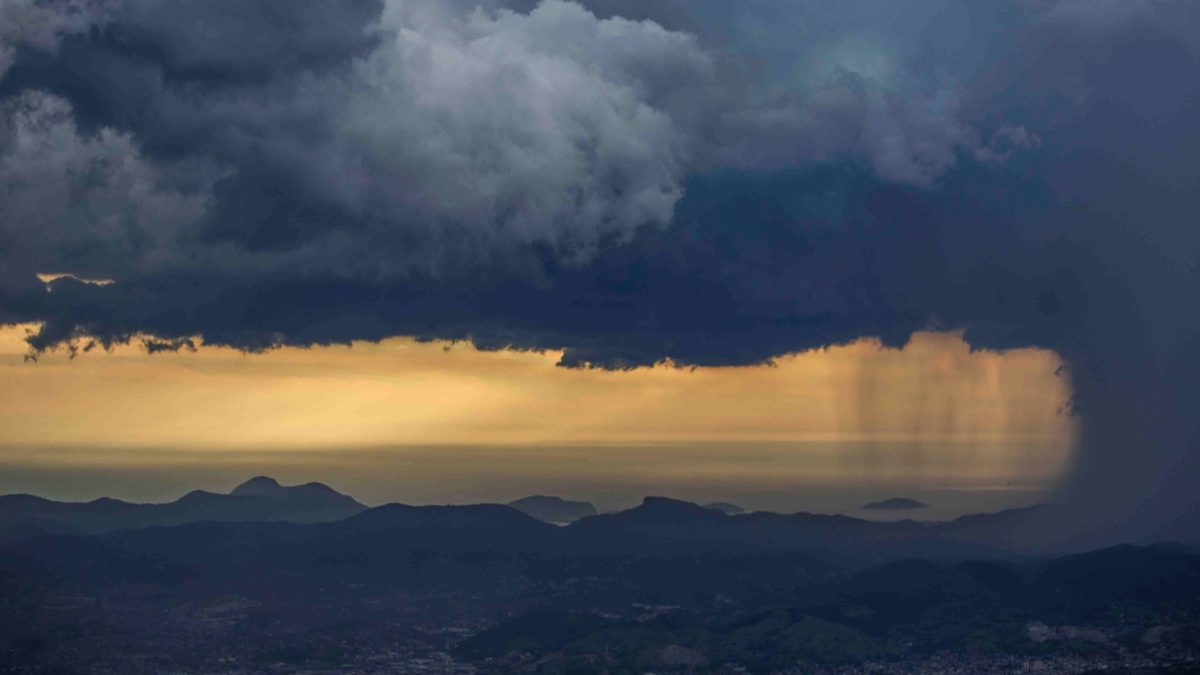 Céu de temporal sobre o Rio de Janeiro à noite, com nuvens carregadas, ao fundo prédios e morros iluminados