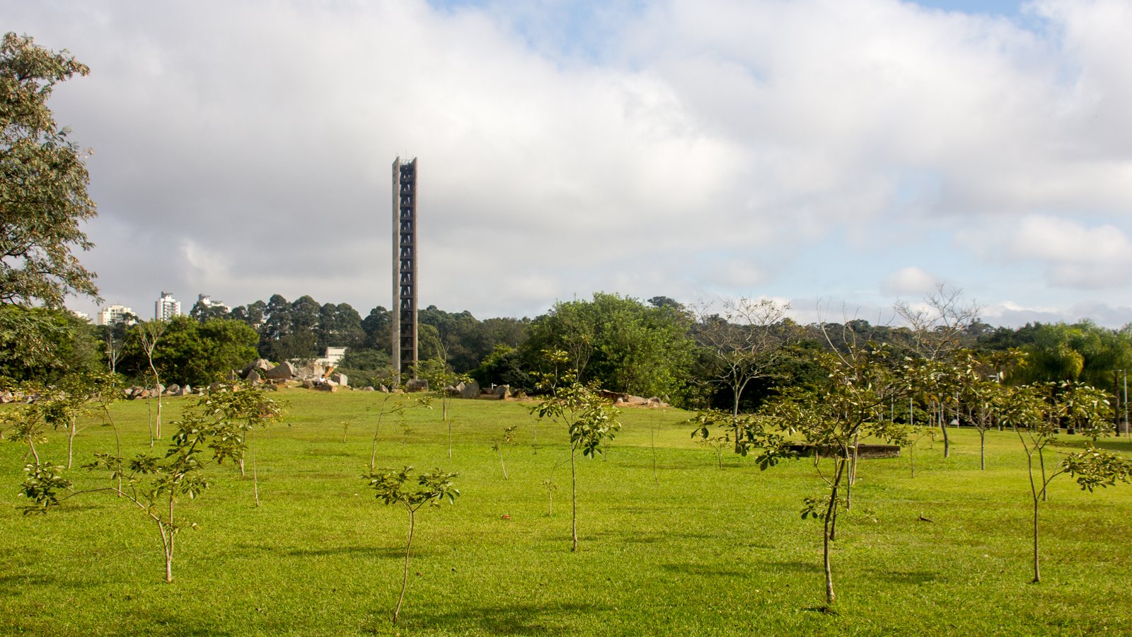 Torre do Relógio na Cidade Universitária da USP, em São Paulo, universidade que ficou em 141º no ranking THE 2027: uma torre alta e estreita de concreto no meio de um gramado com árvores jovens, sob céu com nuvens